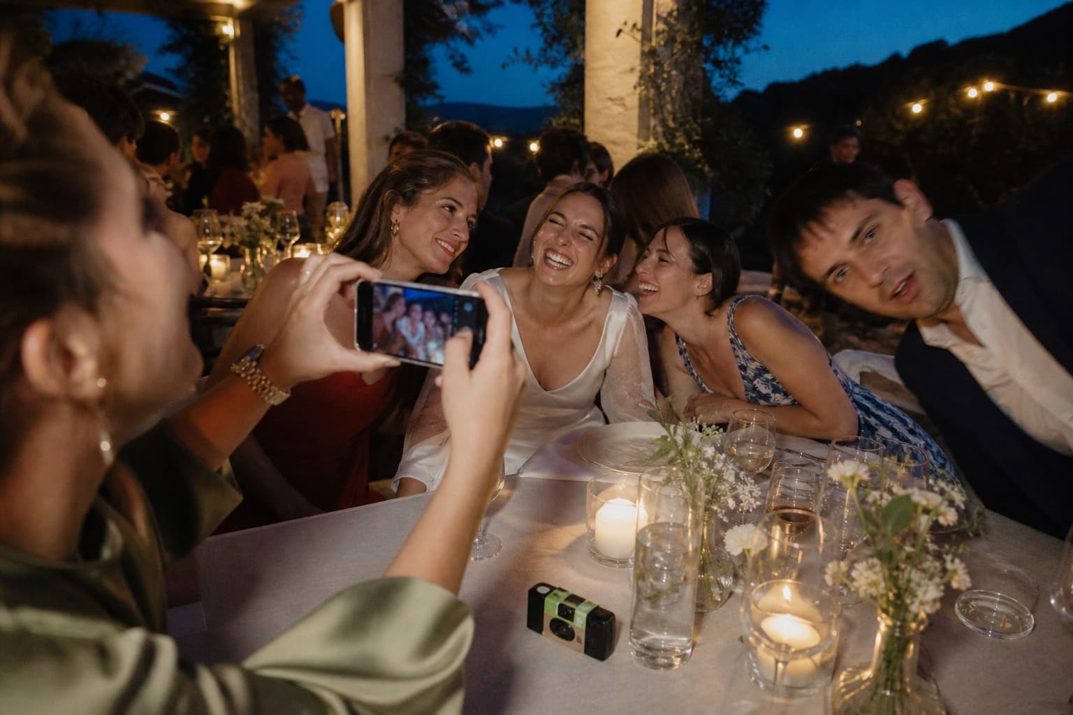 Invitada fotografiando con el móvil un momento espontáneo junto a una cámara desechable durante una boda